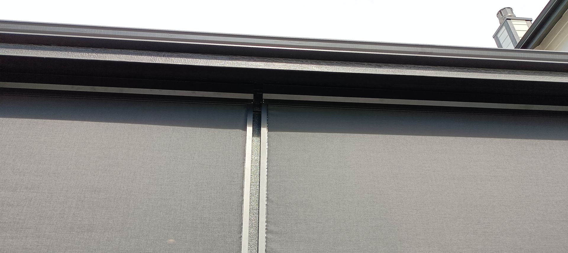 Close-up of a building roof edge with black trim and a vertical seam between two gray panels.