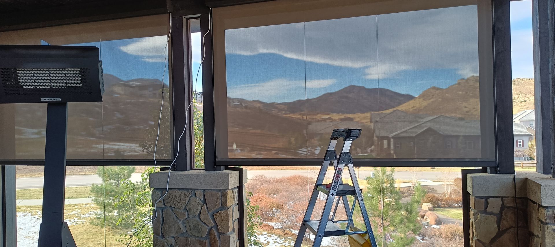 Ladder in front of large window with desert mountains and sky beyond, viewed from indoors