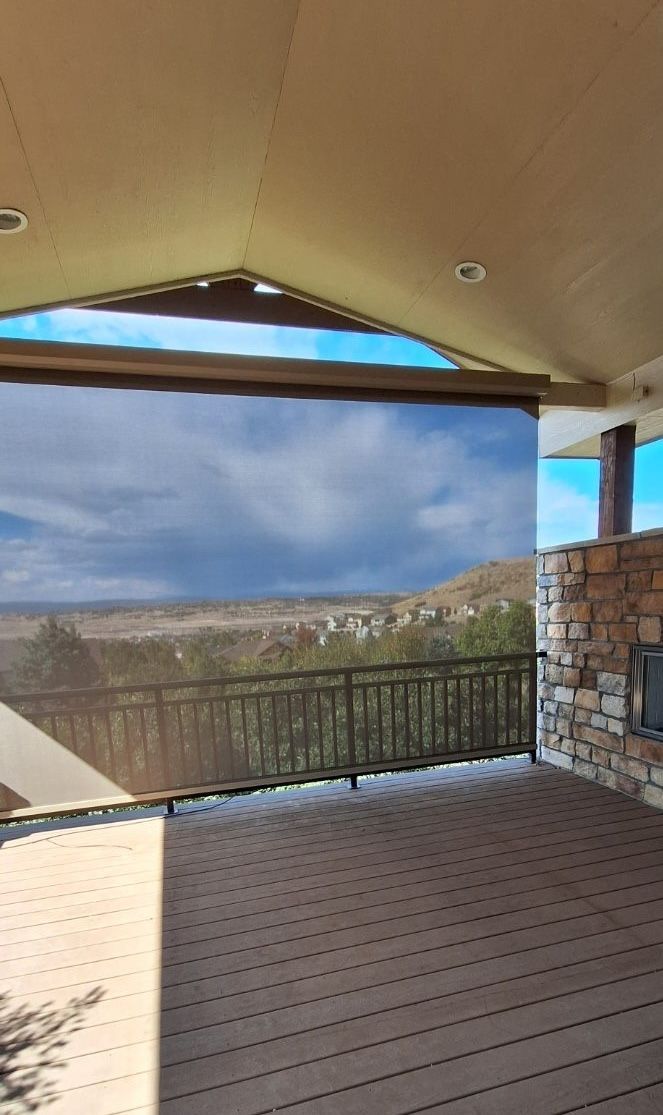 Covered patio with brown deck, stone wall, and mountain view beyond a mesh railing
