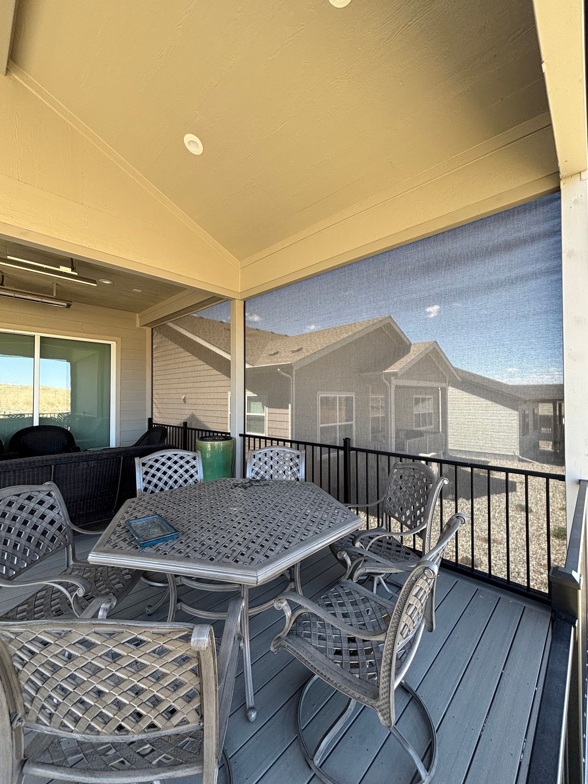 Covered patio with metal table and chairs overlooking neighboring houses and a blue sky