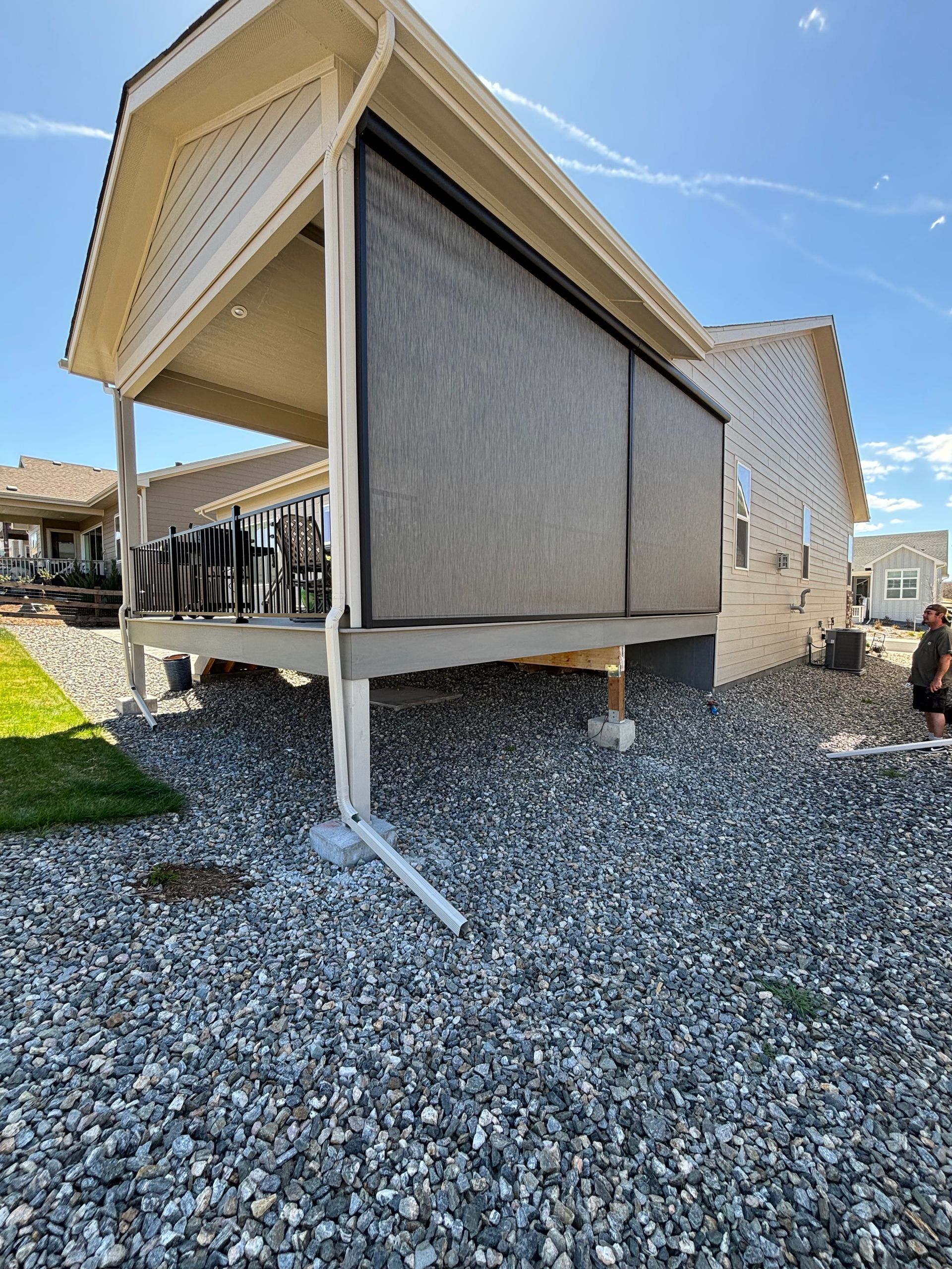 Outdoor covered structure with beige retractable shades on gravel under a clear blue sky
