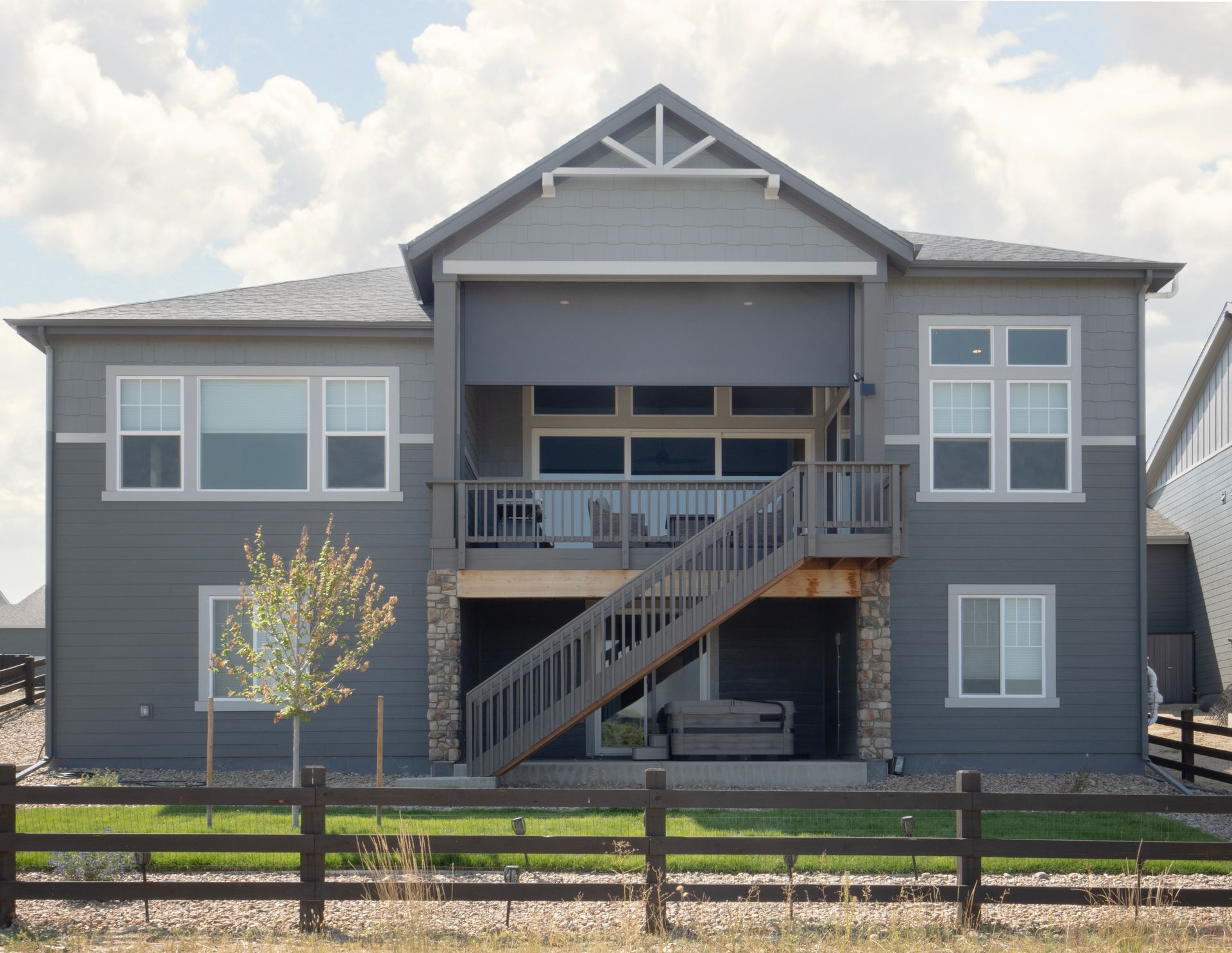 Gray two-story house with front balcony, exterior stairs, and a wooden fence in front