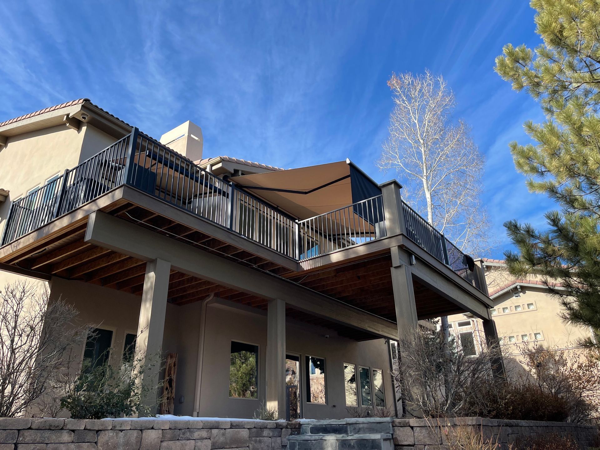 Modern deck on a stucco house with black railings, viewed from below under a blue sky.
