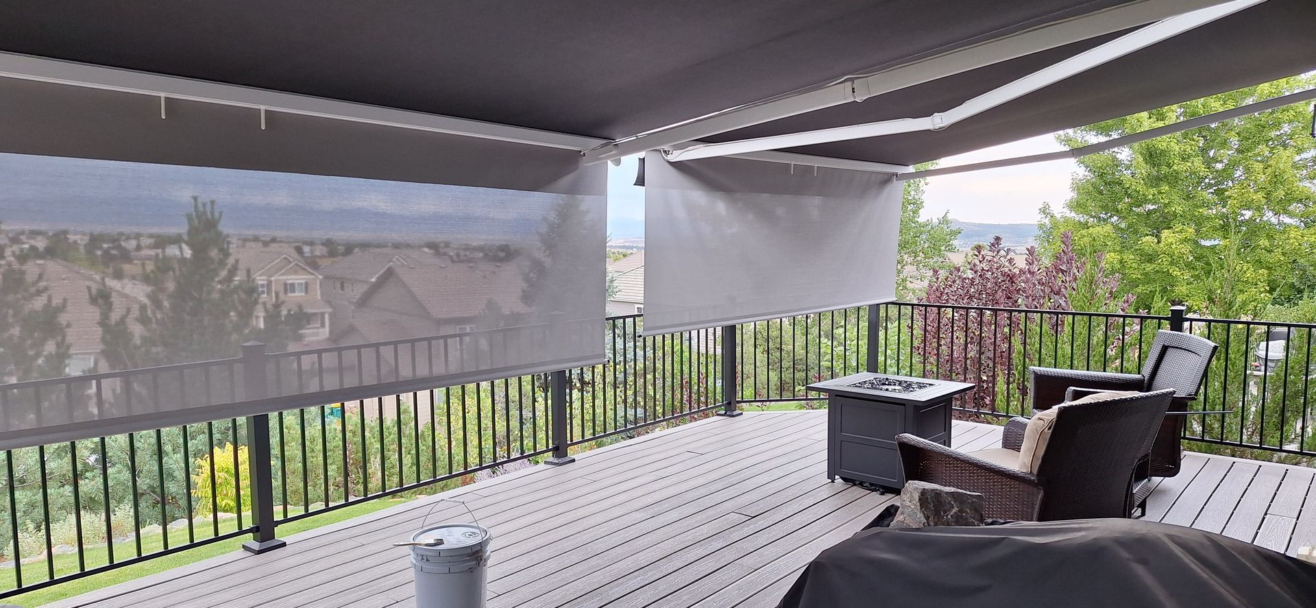 Covered patio with outdoor seating, black railing, and a neighborhood view beyond the mesh screens