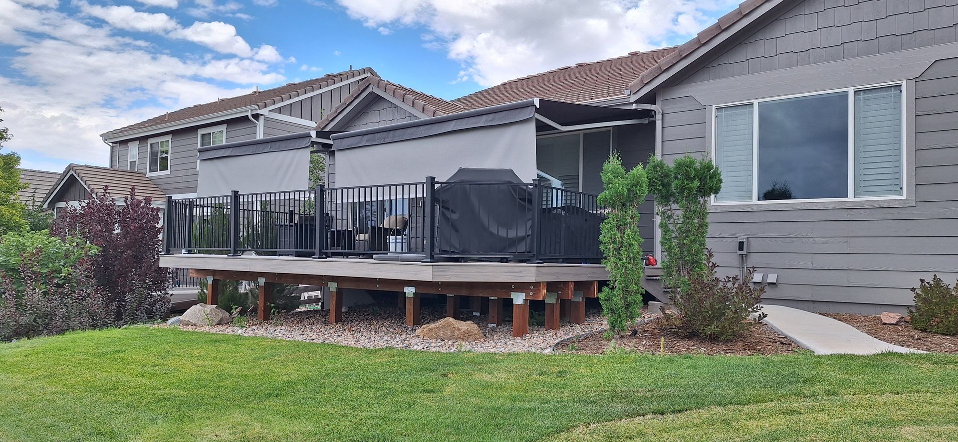 Backyard deck with black railings and patio furniture beside a gray house and green lawn
