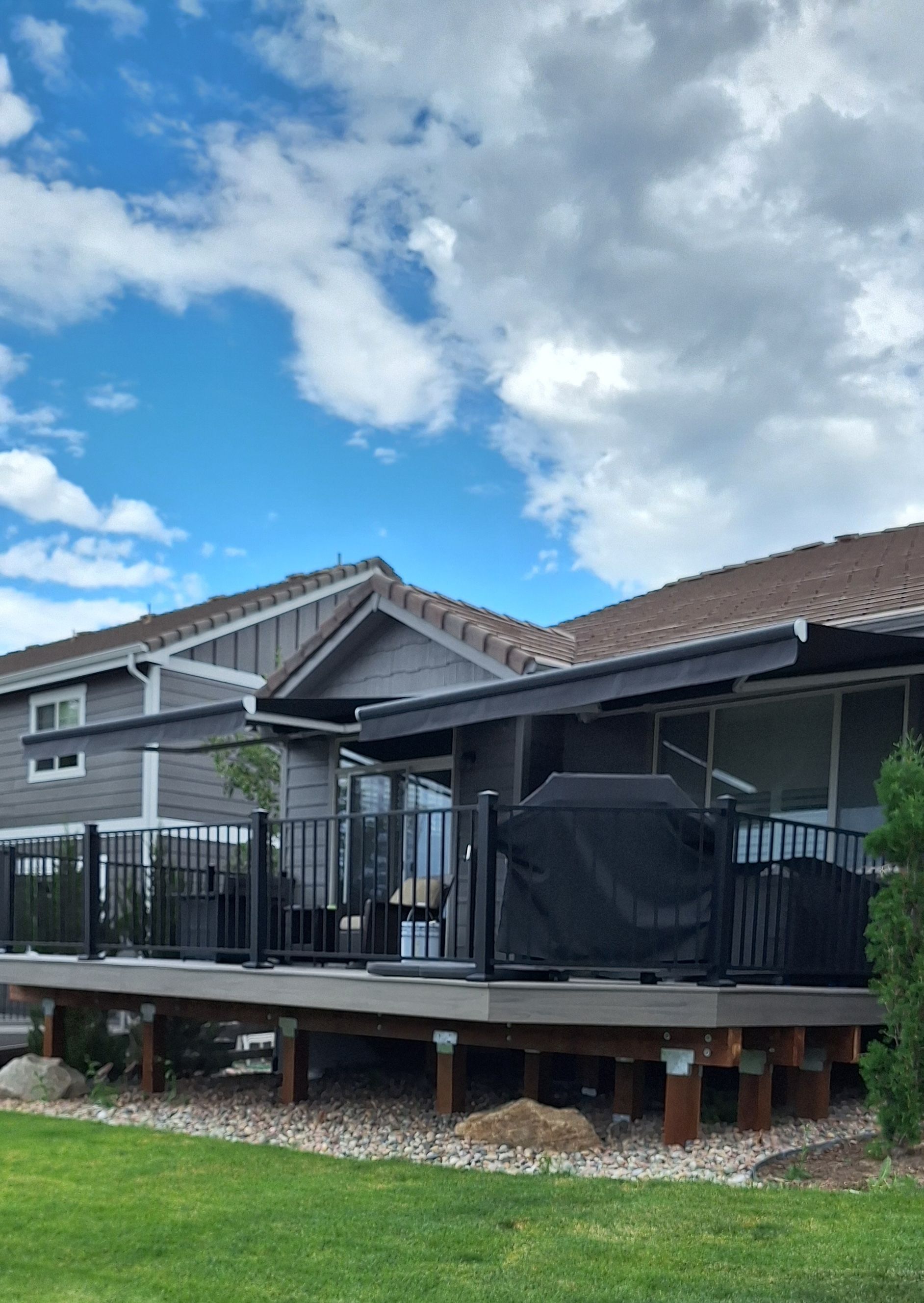 Backyard deck with a covered patio, black railing, and neighboring houses under a partly cloudy sky