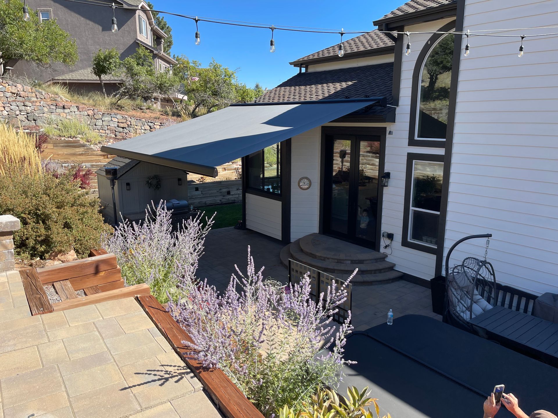 Patio with awning, lavender planters, and glass door beside a white stucco house