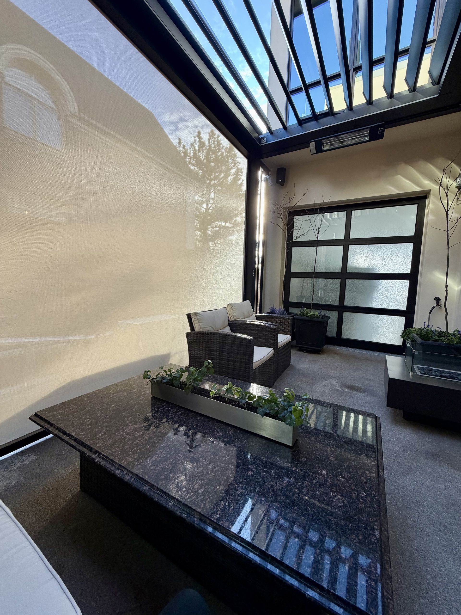 Modern patio seating area with black table, bench, and pergola roof in bright sunlight