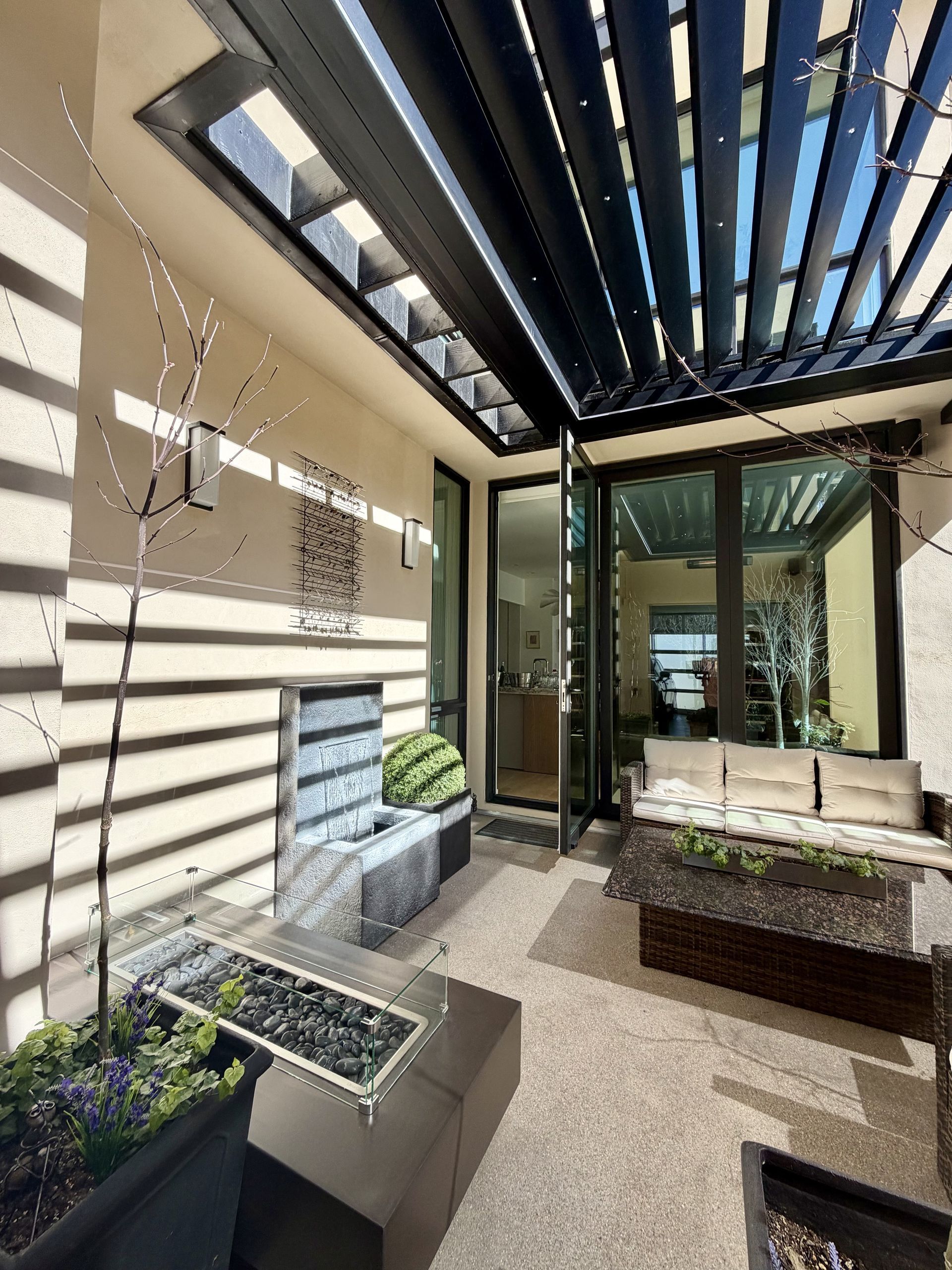 Modern patio with black pergola slats, beige walls, potted plants, and sliding glass doors