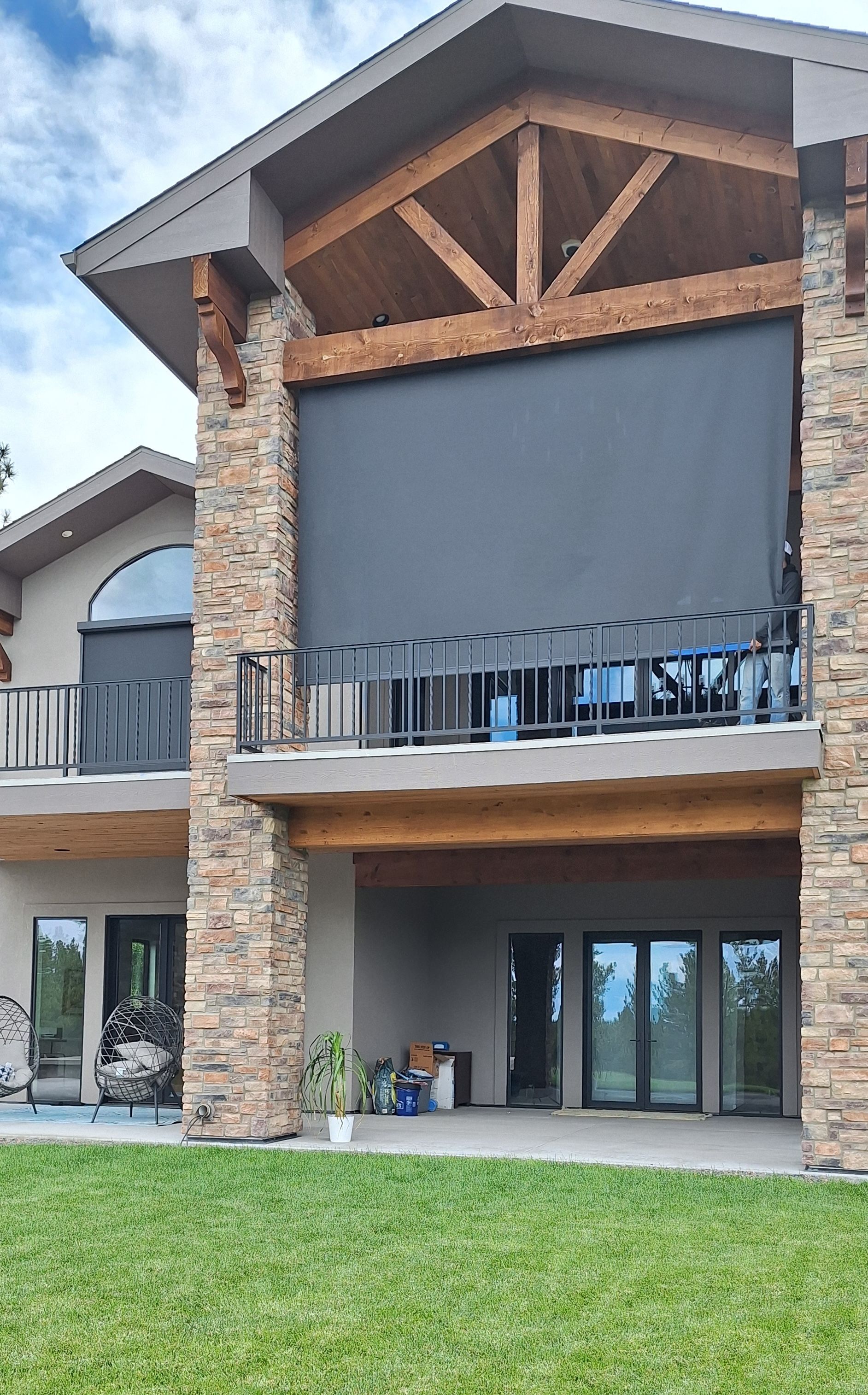 Modern two-story house with stone columns, wood accents, large balcony, and a grassy lawn