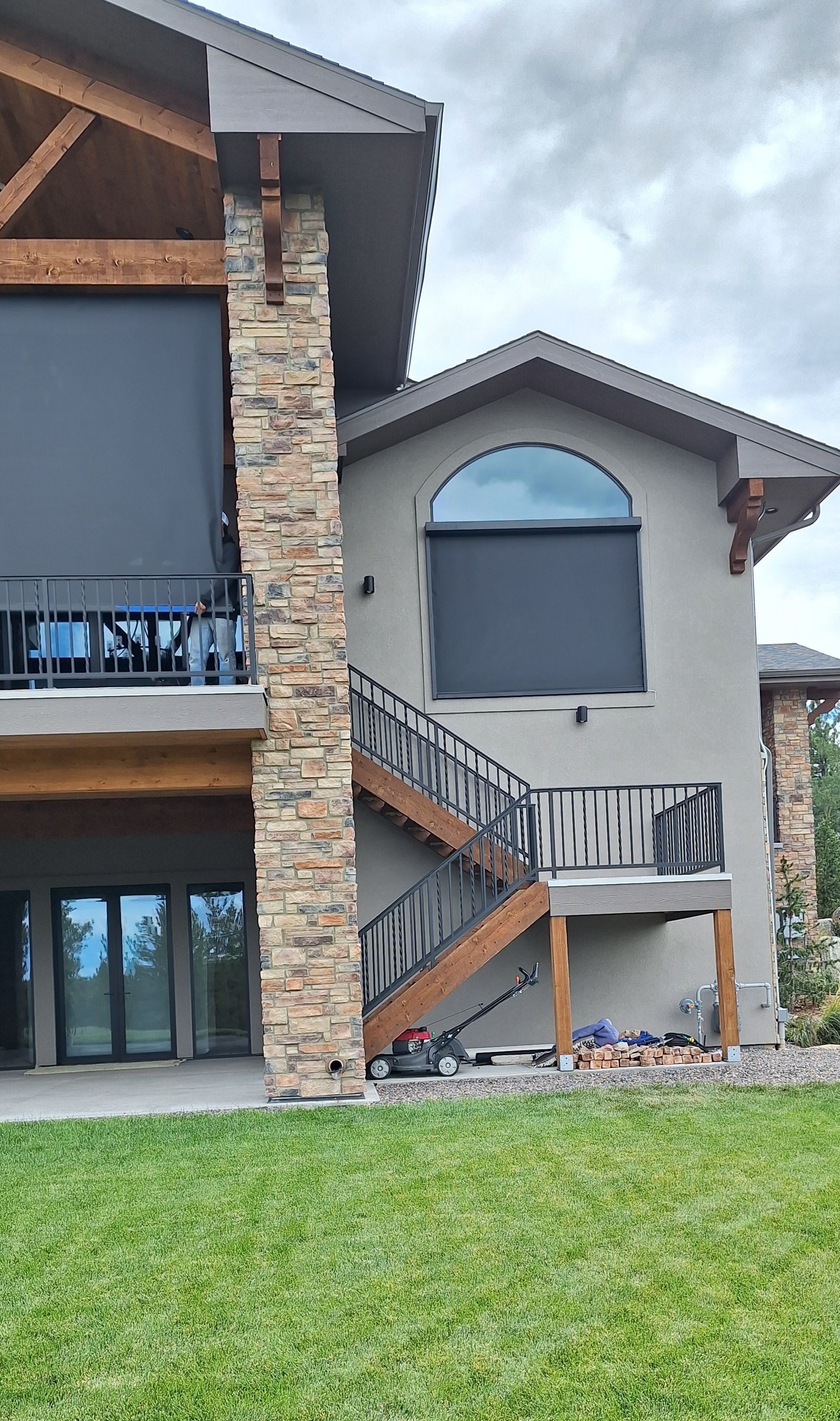 Modern stone-and-wood house exterior with balcony, stairs, and a large arched window under a cloudy sky