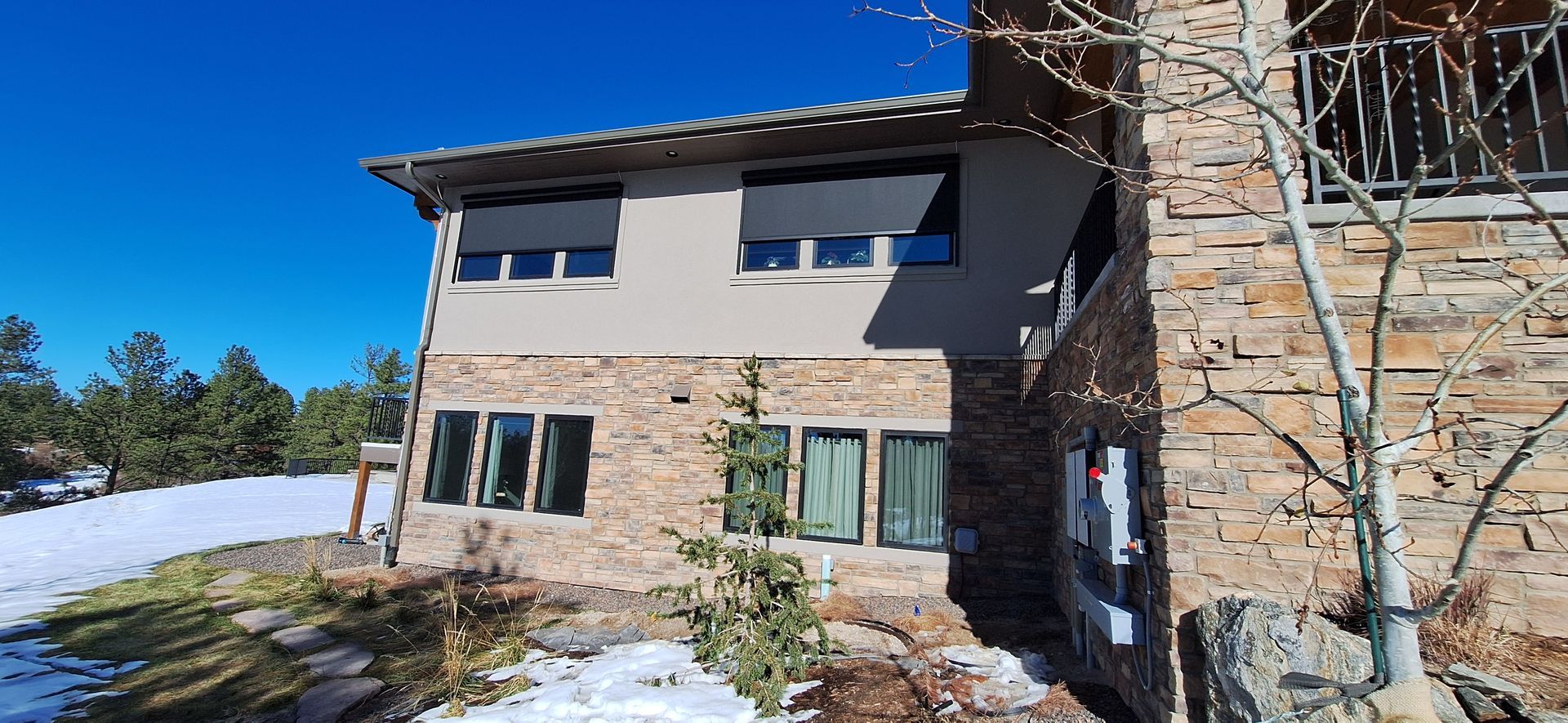 Snowy house exterior with stone and stucco walls, balcony, and blue sky