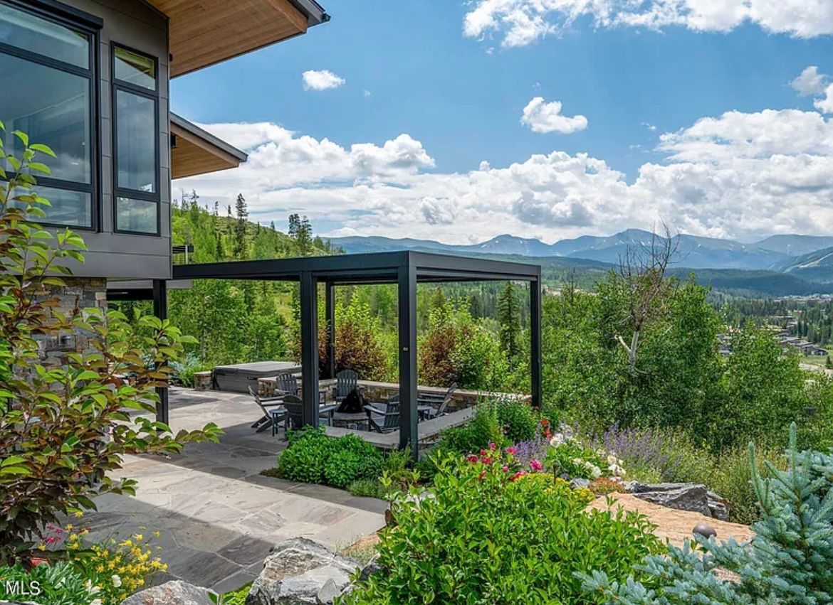 Modern home patio with garden seating, lush greenery, and mountain views under a blue sky