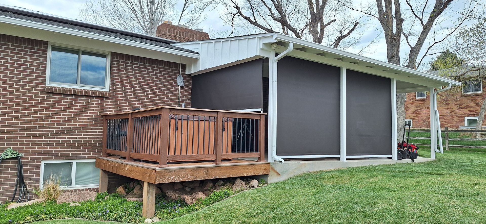 Backyard deck with wooden railing beside a brick house and screened patio under trees