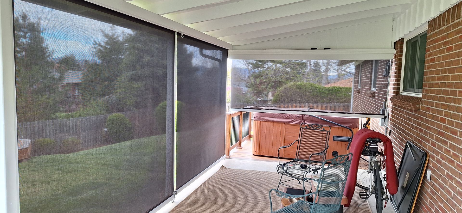 Covered porch with screened enclosure, red ladder, stacked chairs, and storage bins beside a brick wall