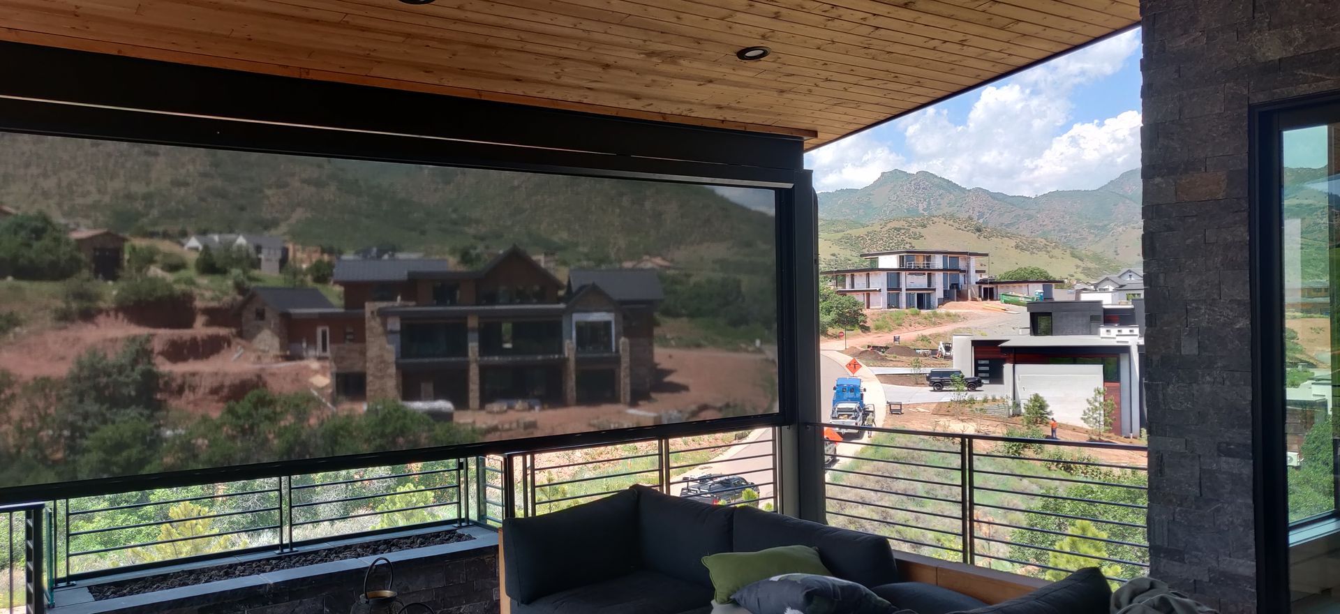 Covered balcony with outdoor seating overlooking houses and mountains through mesh shade screens.