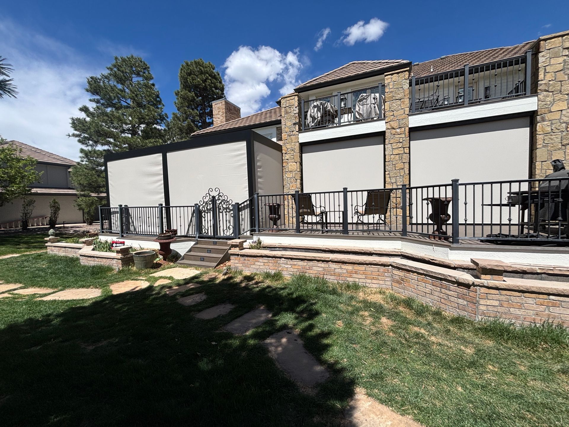 Backyard patio with white privacy screens, black railings, stone steps, and a grassy yard under a blue sky
