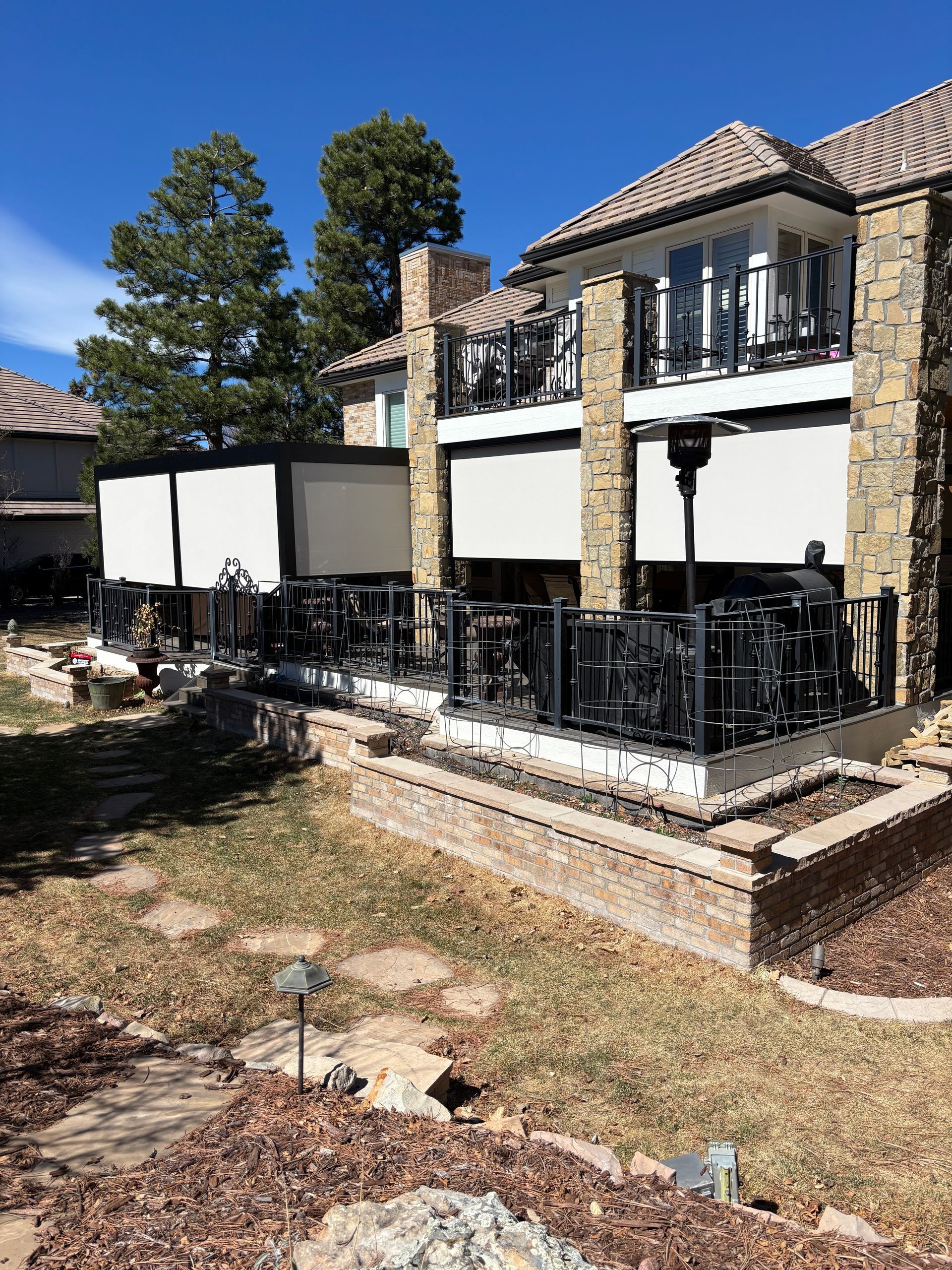 Two-story townhouse with black balcony railings, white privacy panels, and a dry yard under clear blue sky