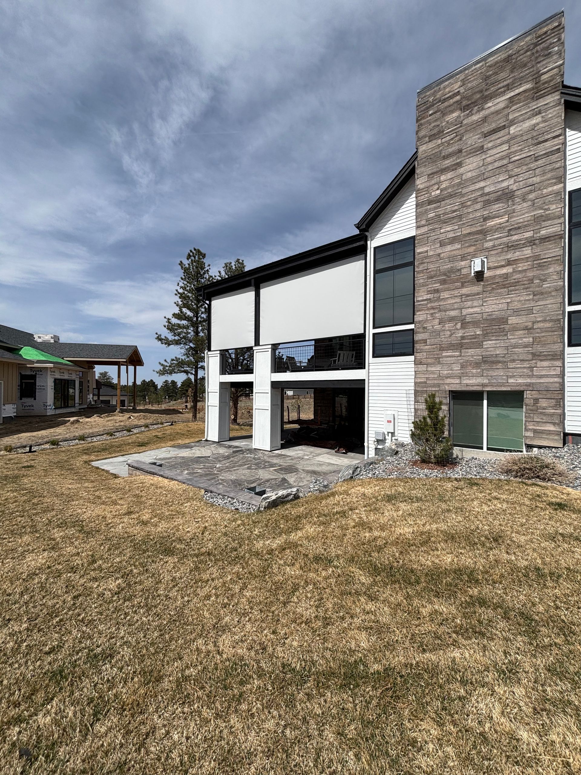 Backyard view of a modern two-story house with brick, white siding, and dry grass lawn