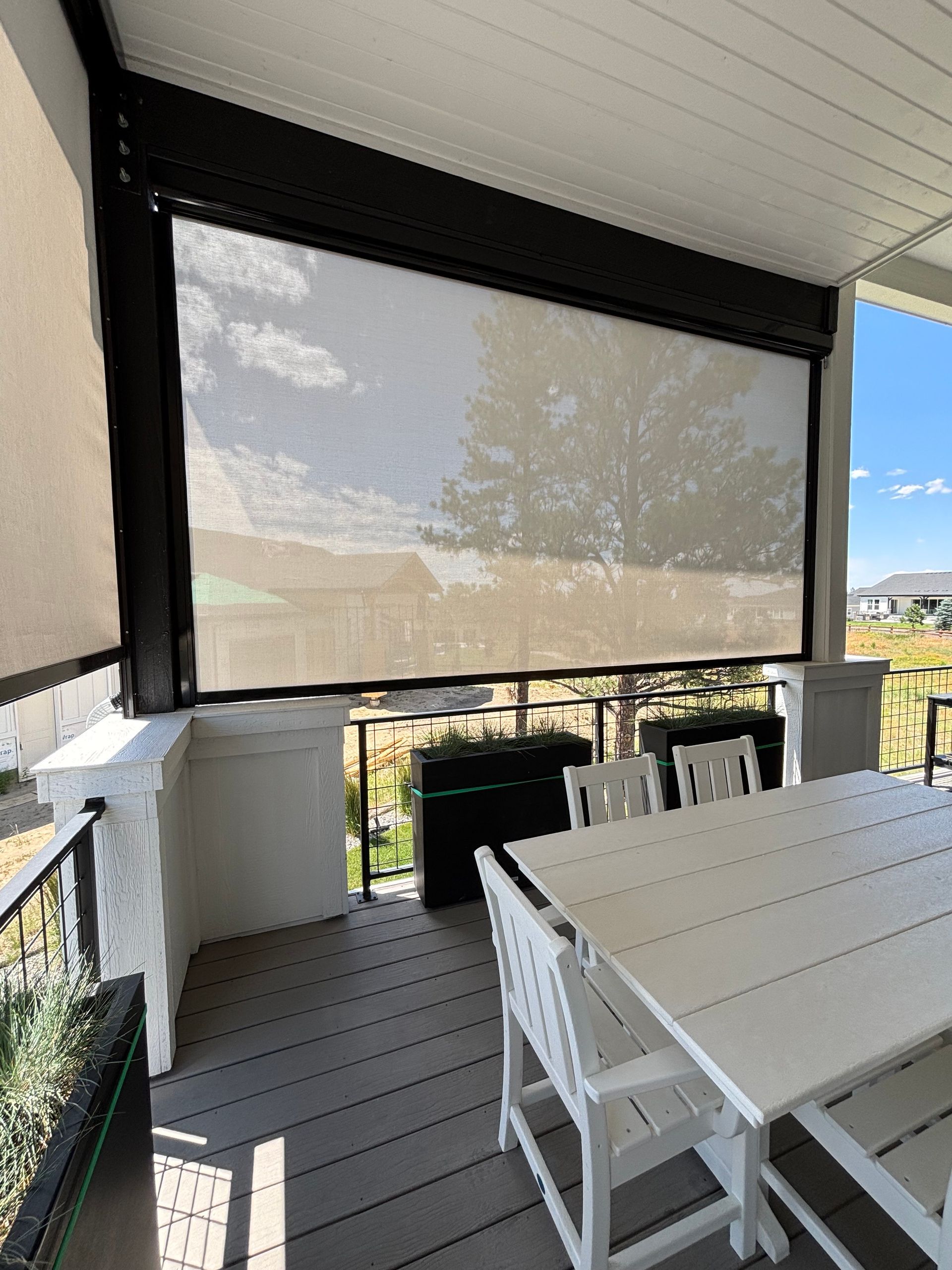 Covered patio with white outdoor table and chairs, dark screened drop shade, and a view of the yard beyond.