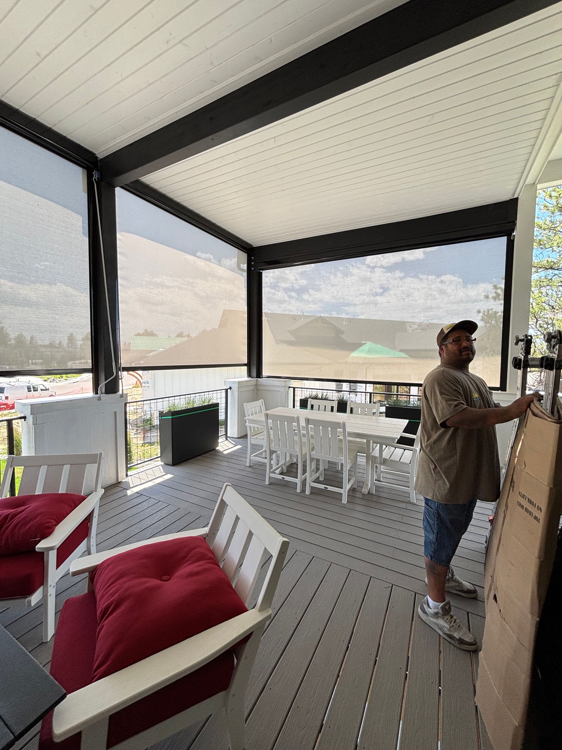 Covered patio with white chairs, red cushions, and a person standing by a wall, overlooking a coastal view.
