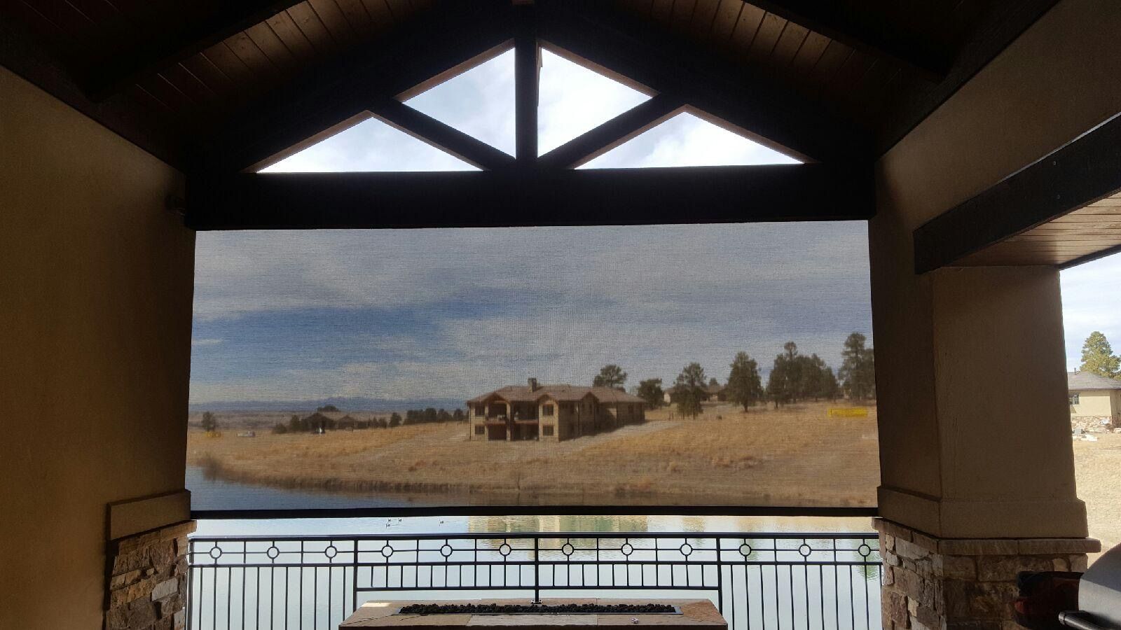 Covered patio framing a calm lake, wooden dock, and grassy shoreline under a cloudy sky.