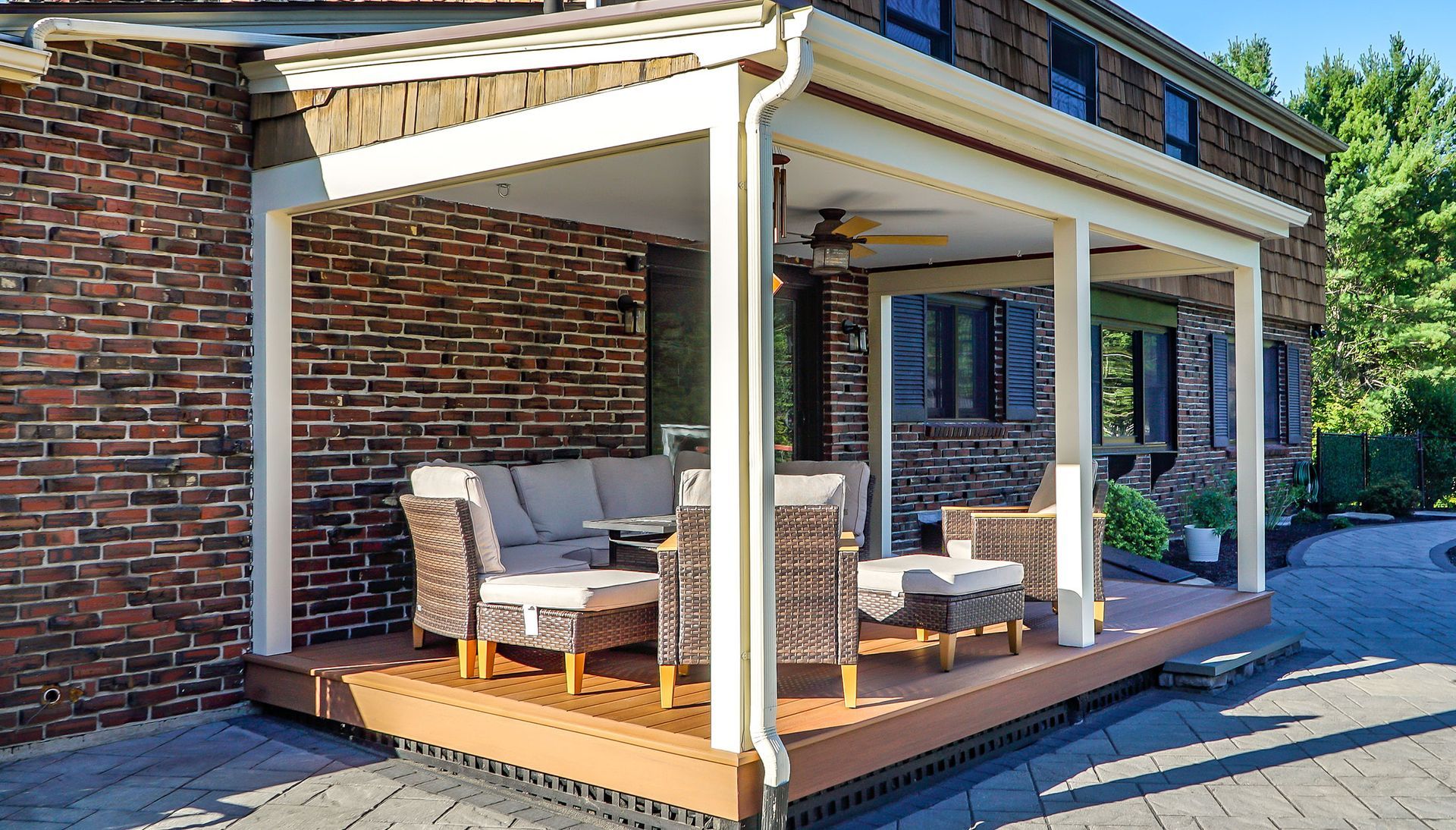 Covered brick patio with outdoor dining table, chairs, and lounge seating in bright sunlight.