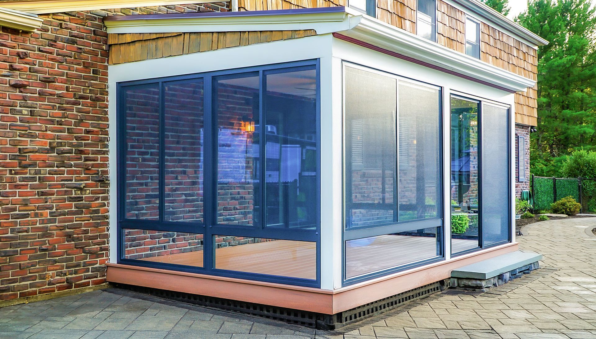 Modern glass-enclosed patio extension with blue-framed windows beside a brick house.