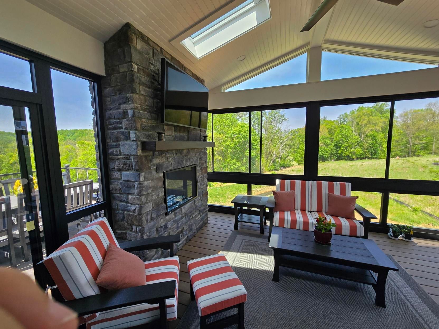 Sunroom porch with stone fireplace, black patio furniture, and red-and-white striped cushions overlooking trees
