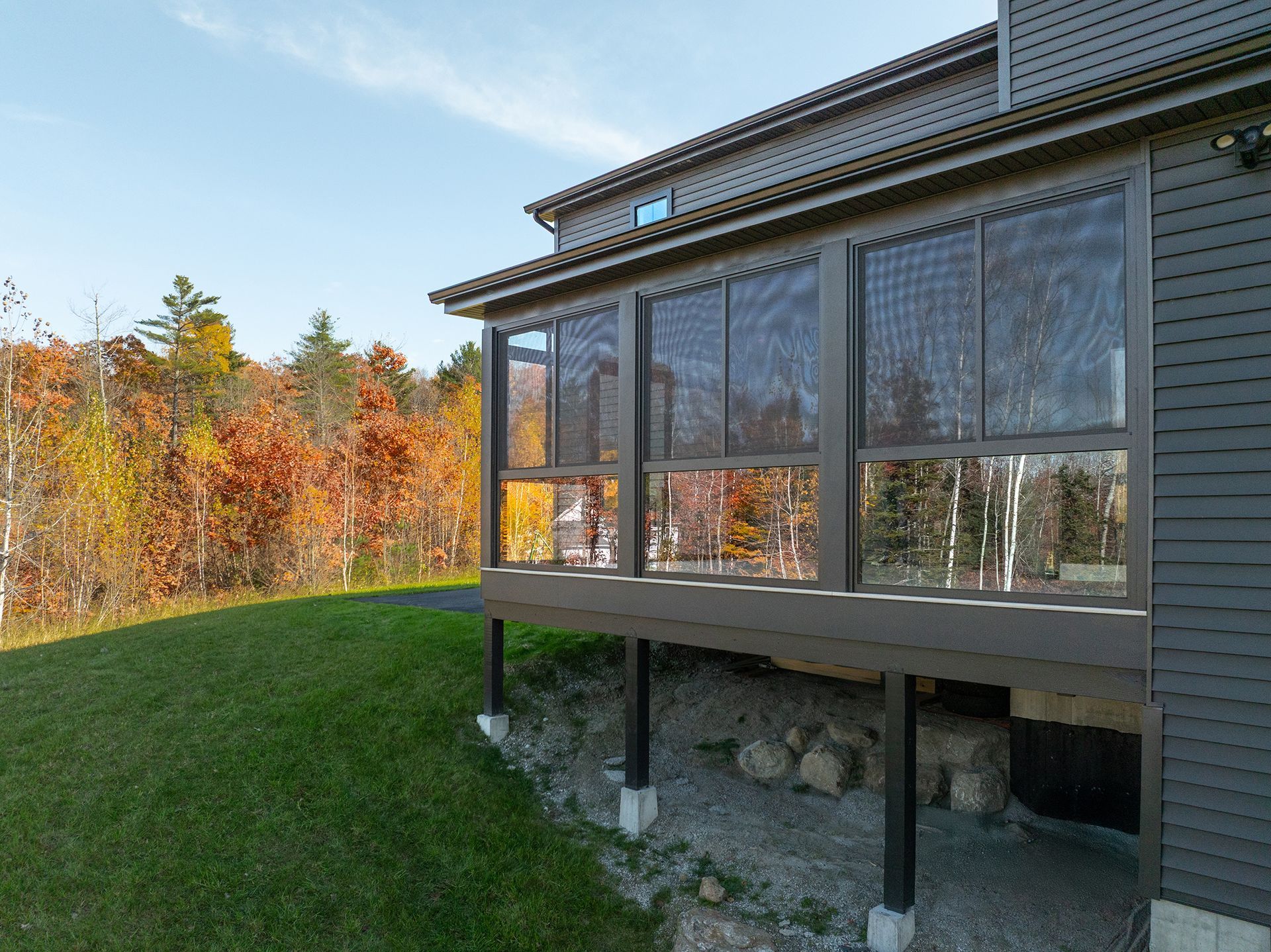Modern house with a screened porch overlooking a grassy yard and autumn trees