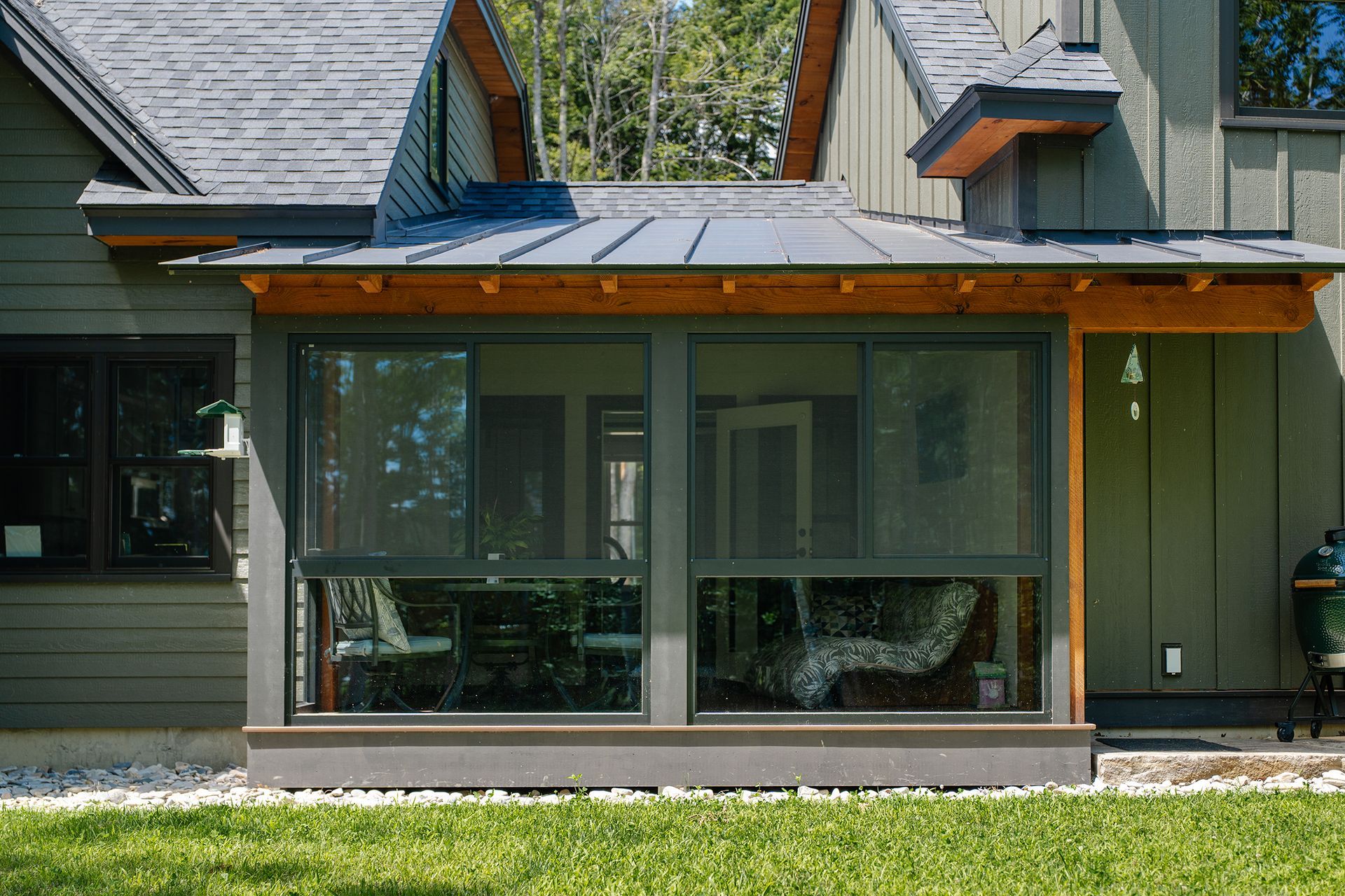Modern house exterior with a large glass sunroom and metal roof, fronted by green lawn