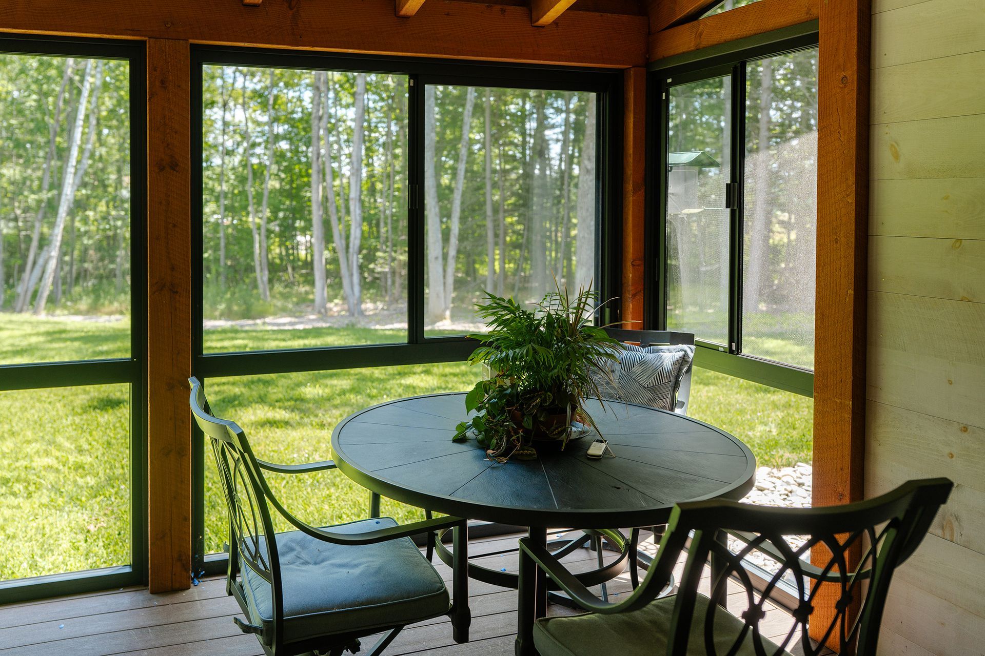 Sunroom with round table and chairs overlooking a green lawn and trees through large windows