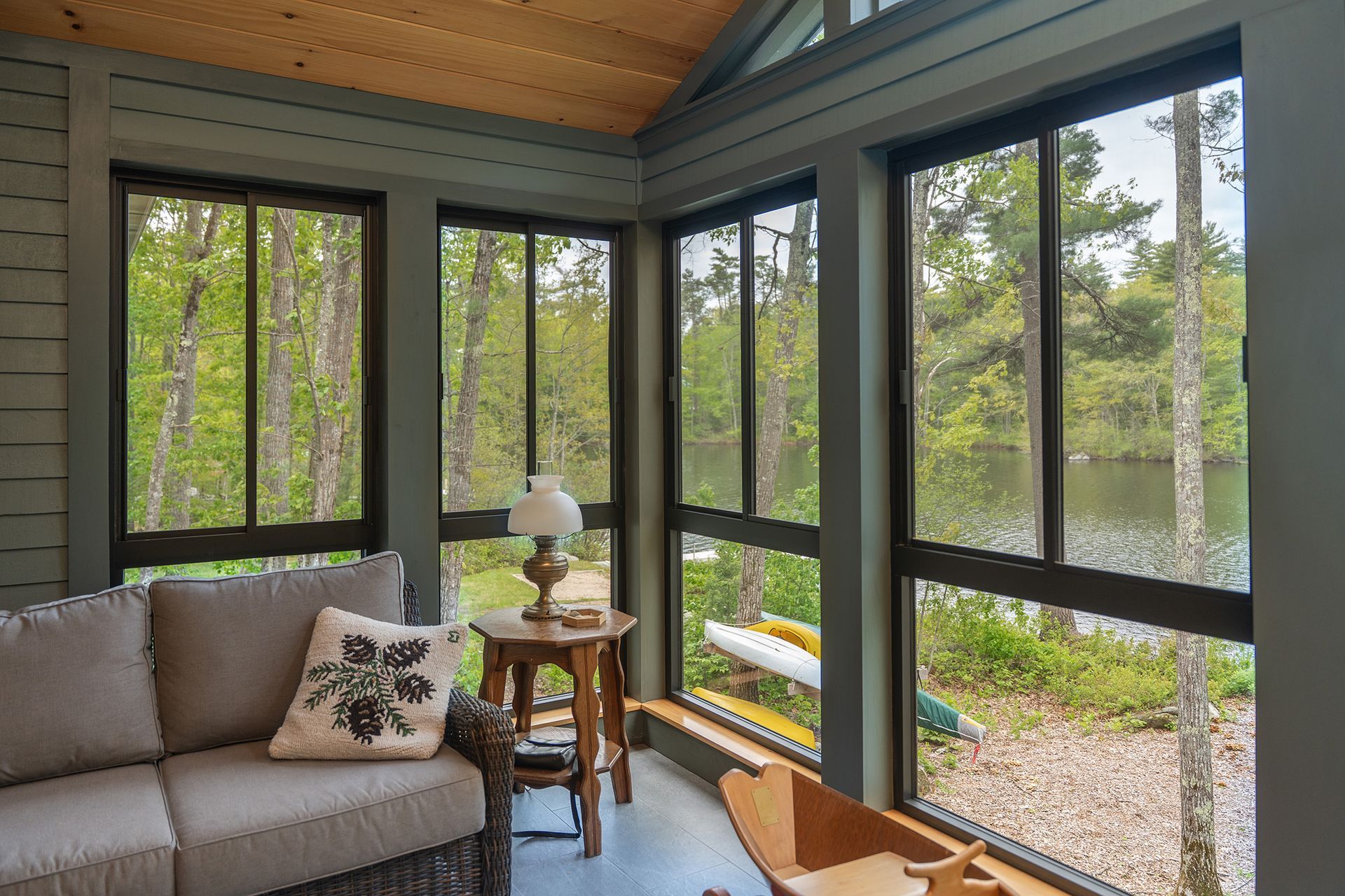 Sunroom with black-framed windows, gray sofa, and a small side table overlooking a green yard