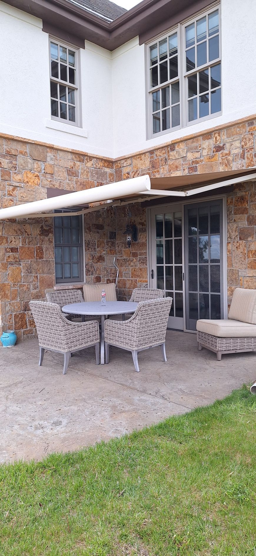 Patio with outdoor dining table and chairs beside a stone house with sliding glass doors