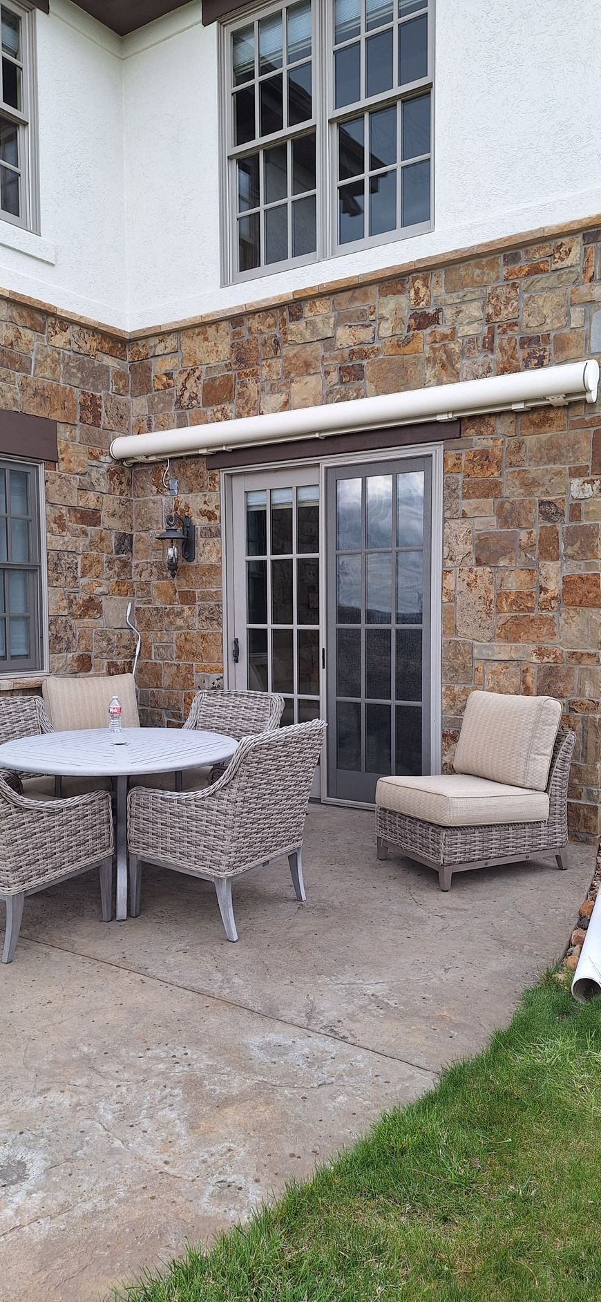 Stone patio with wicker outdoor table, chairs, and bench beneath a windowed brick wall