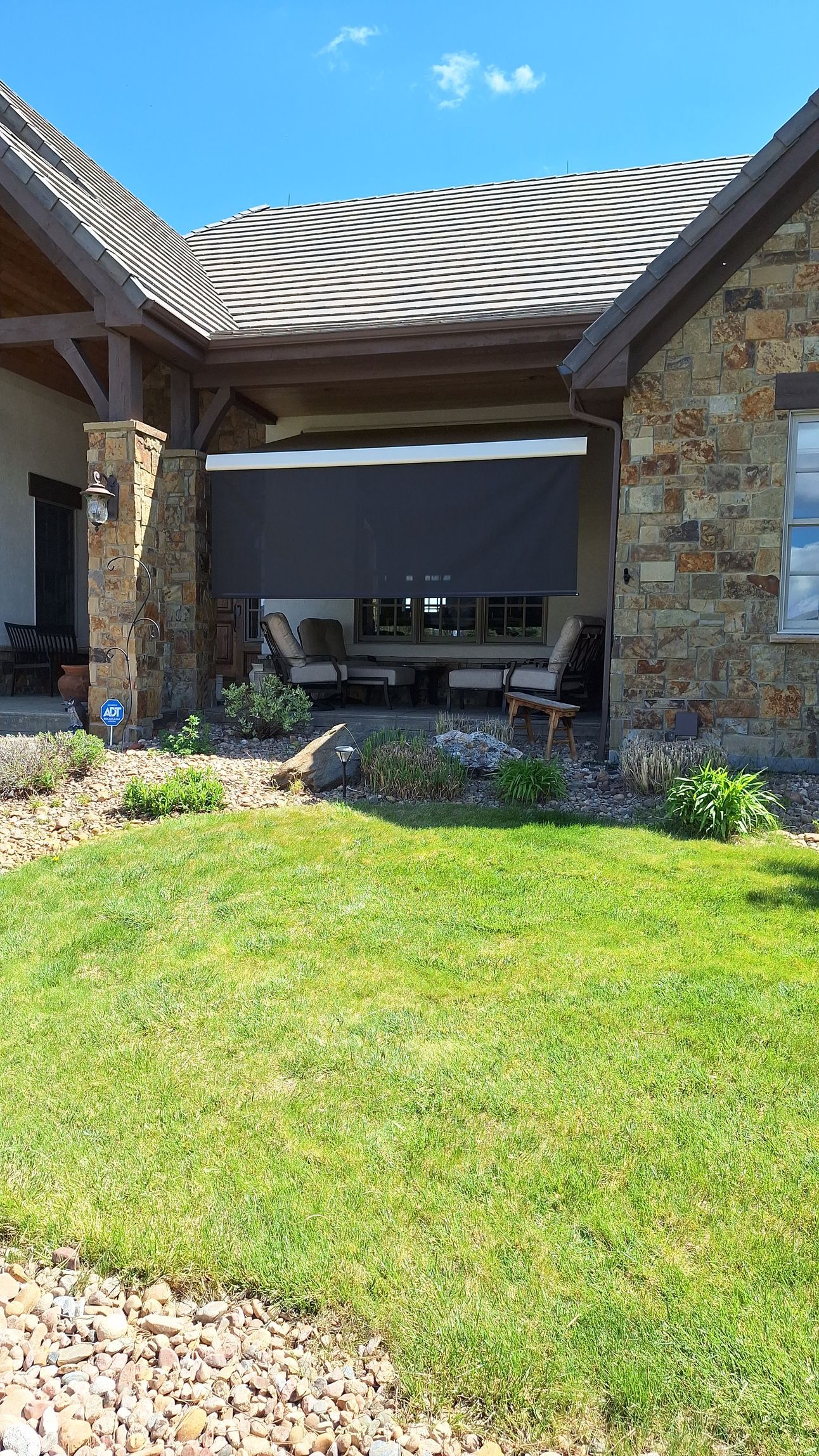 Stone patio with shaded pergola, green lawn, and garden landscaping outside a home