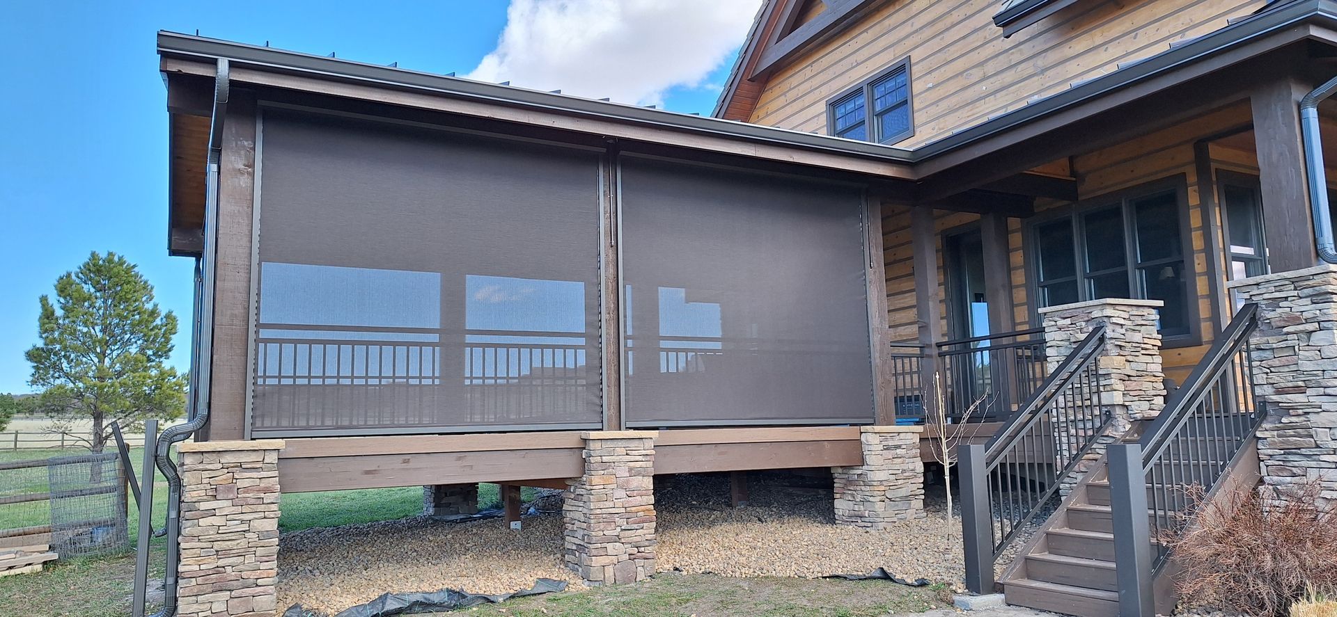 Modern house exterior with screened porch, stone pillars, and front stairs under a blue sky