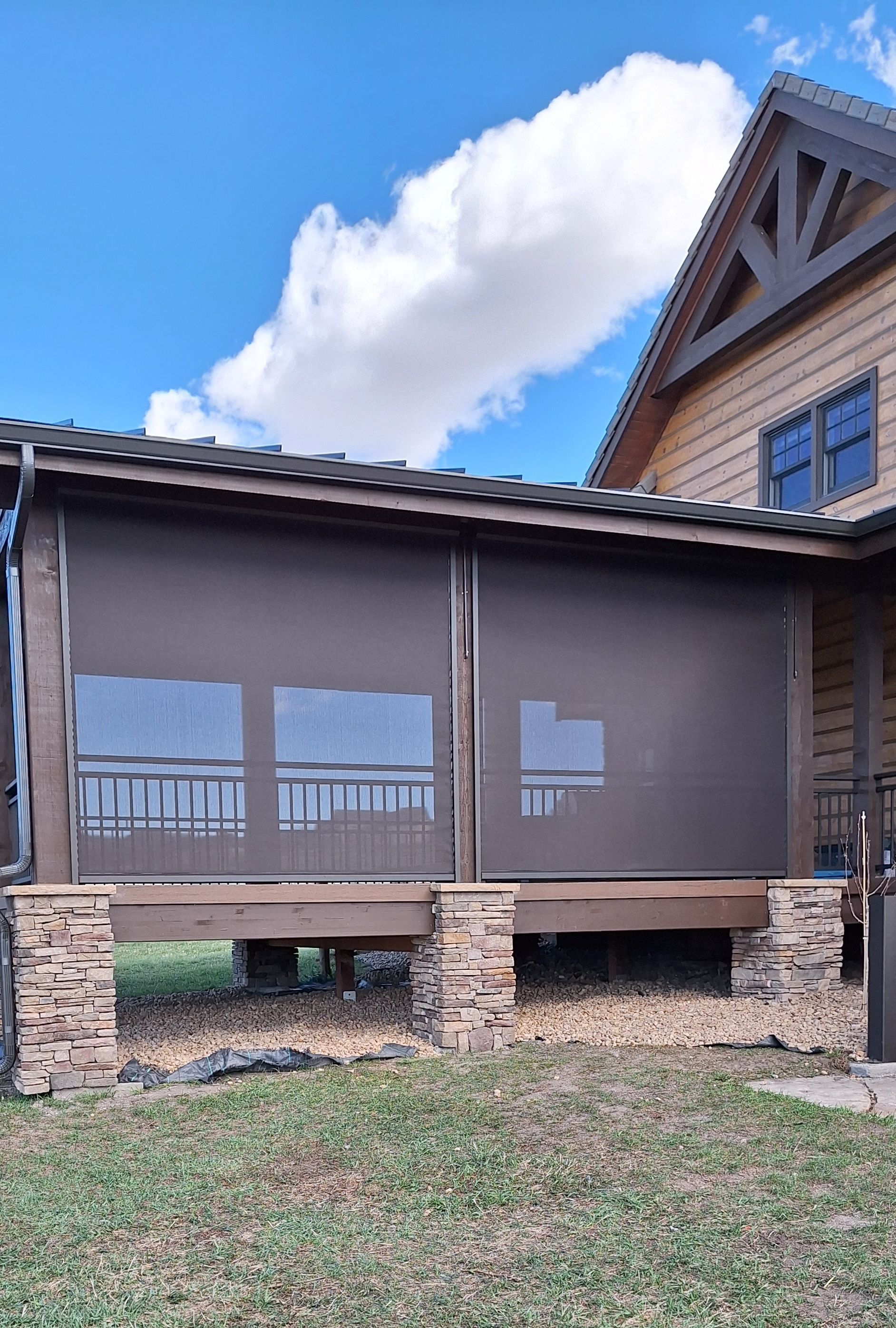Screened porch with dark gray curtains beside a rustic wood house under a blue sky