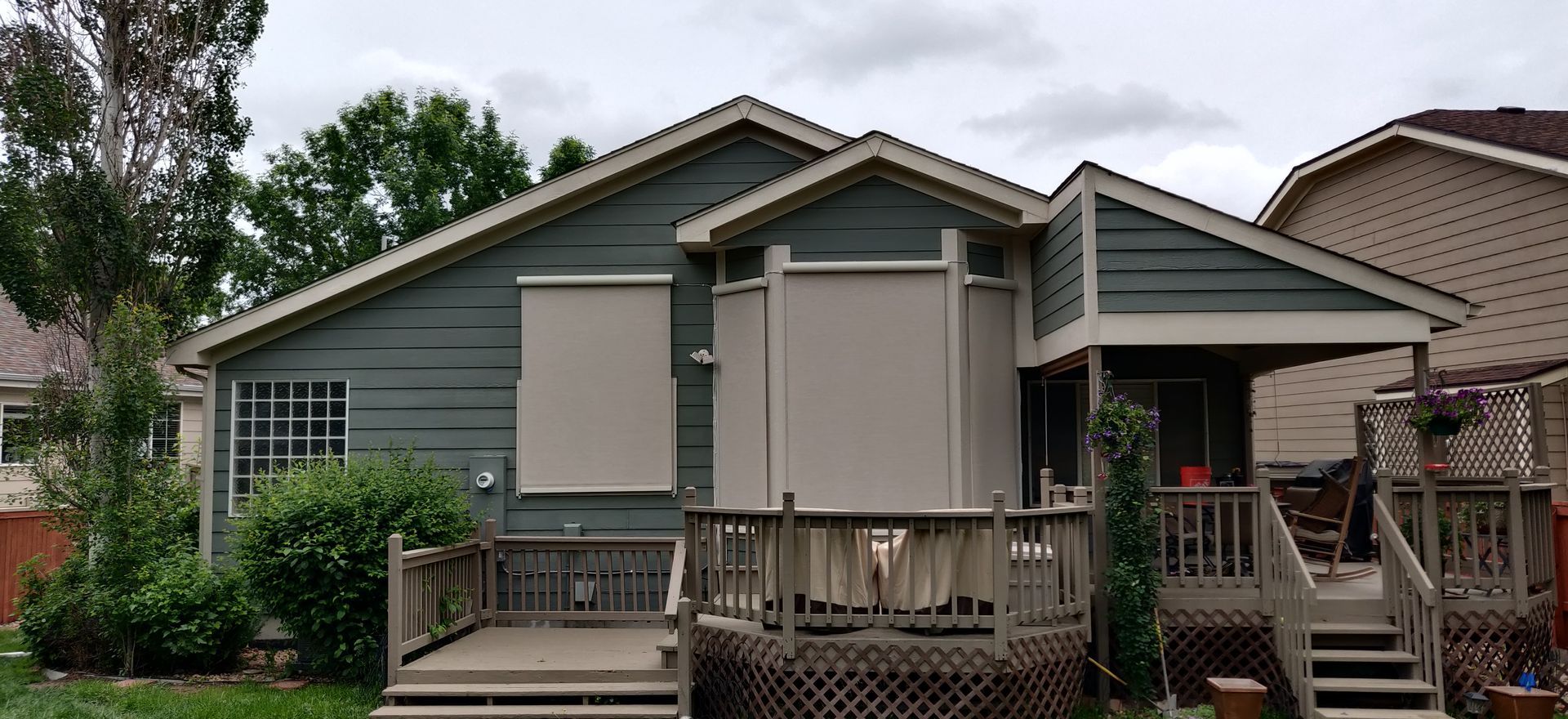 Small gray house with a wooden porch and closed window shutters in a residential yard