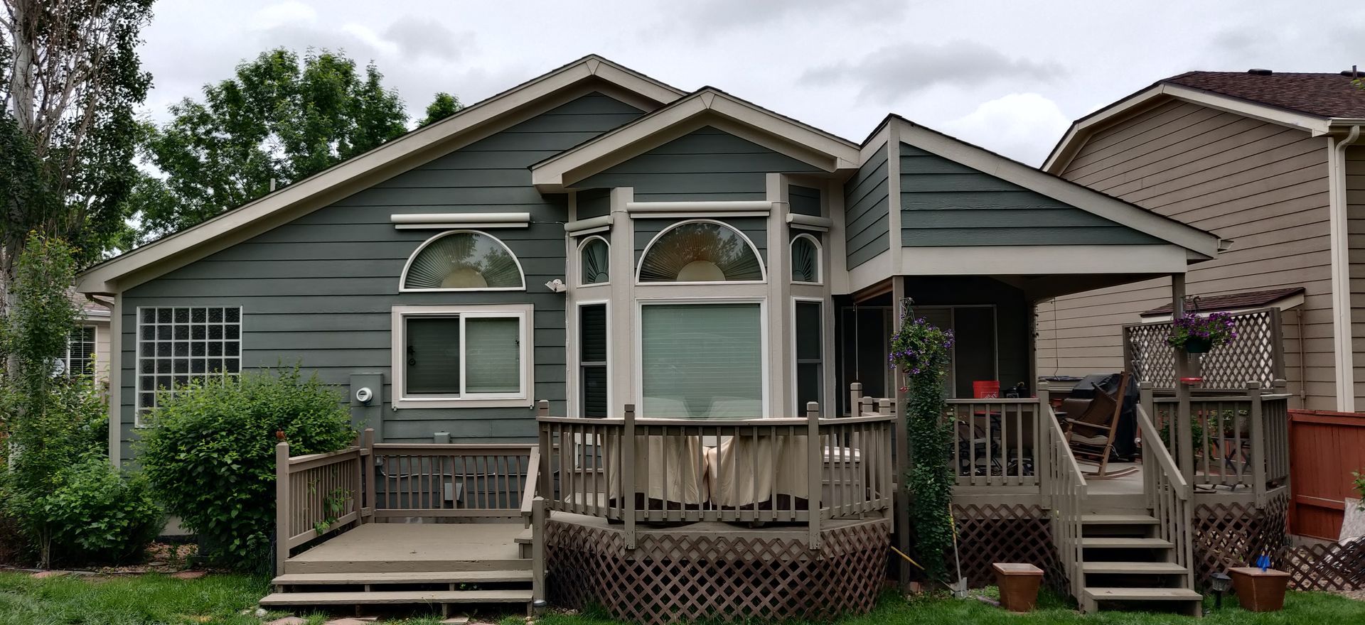 Gray house with front porch, deck steps, and surrounding greenery under cloudy sky