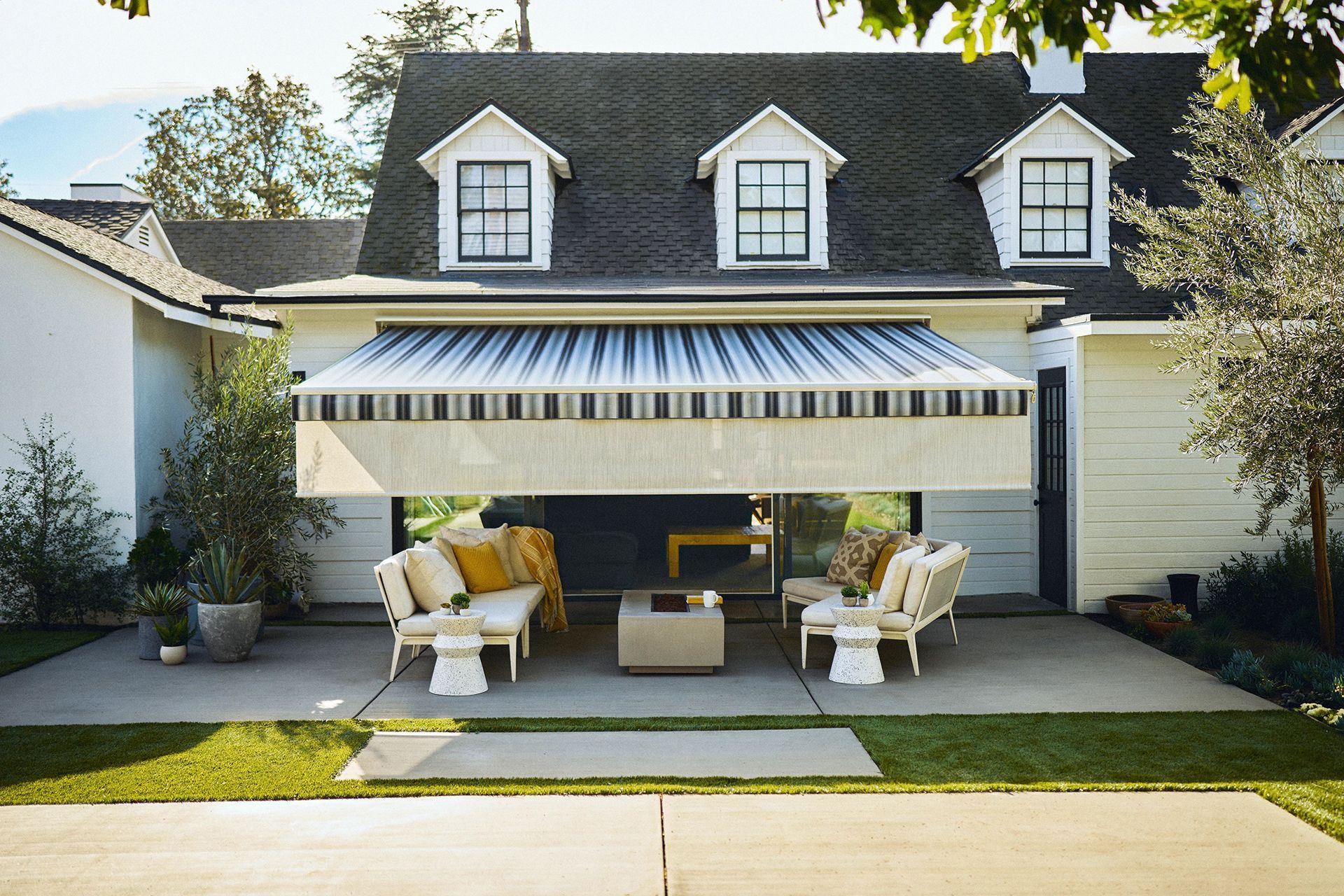 House with striped awning over a cozy front porch, white chairs, and neatly trimmed lawn.