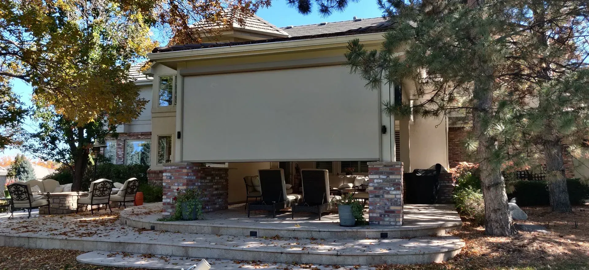 Outdoor patio with a large blank projection screen under trees and a stone terrace