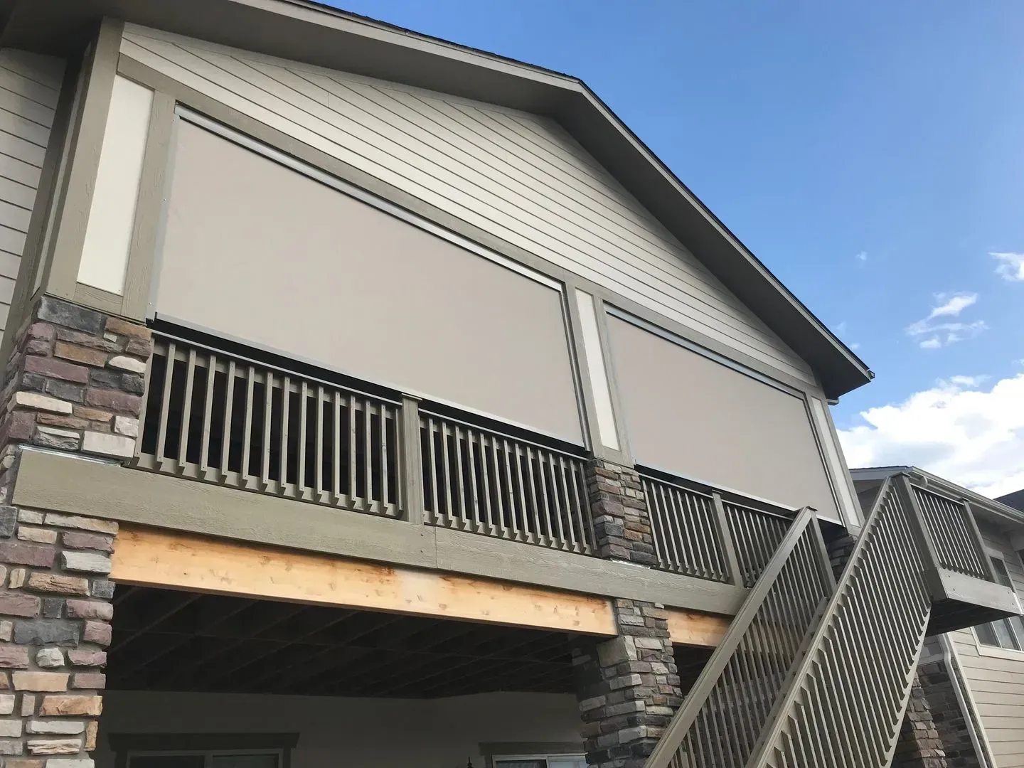 Exterior of a house with stone siding, balcony railing, and a slanted staircase under a blue sky