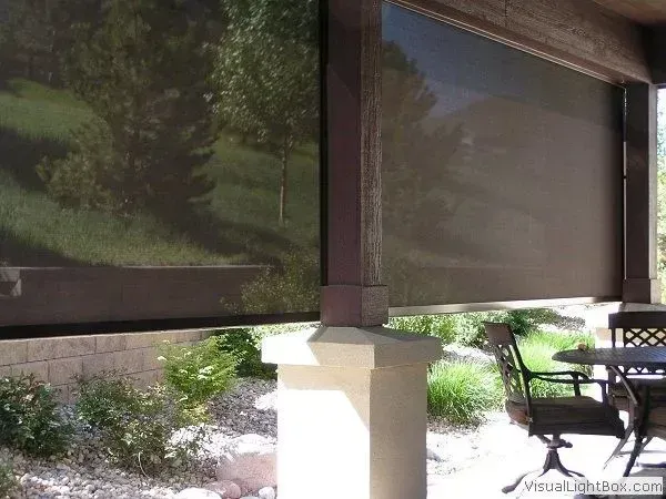 Patio with roll-down shades, wooden posts, and outdoor table and chairs in a sunny garden setting