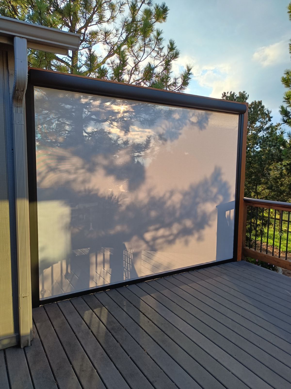 Outdoor deck with a retractable sun shade, blocking sunlight, trees in background.