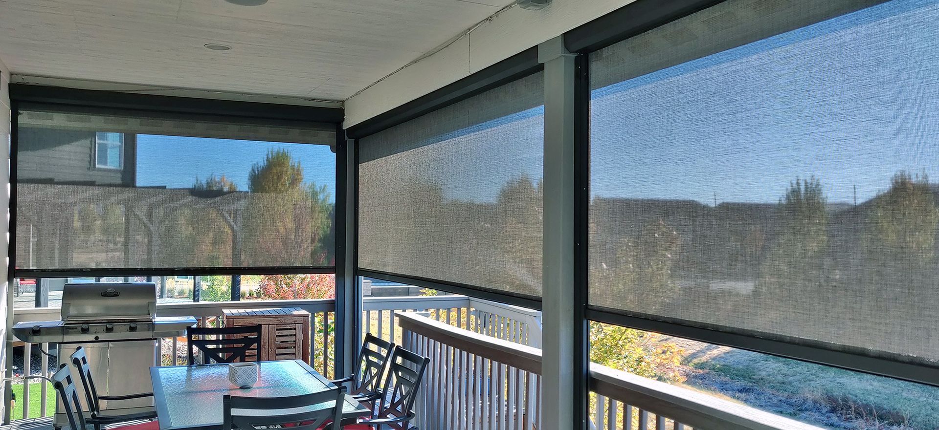 Outdoor covered patio with black roller shades partially lowered to reduce glare.