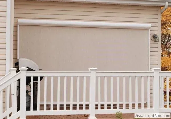 Beige enclosed porch with roll-down shade and white railing in front of house