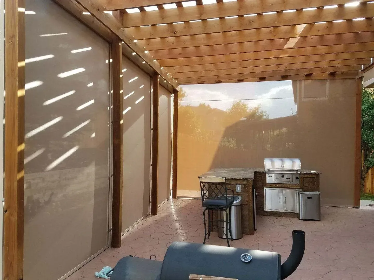 Covered patio with wood pergola, grill, and outdoor sink beside beige privacy screens