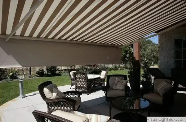 Shaded patio with wicker chairs, round table, and striped awning beside a lawn