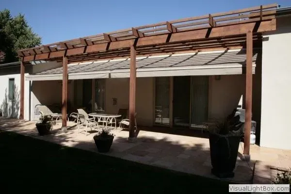 Patio with wooden pergola, white outdoor furniture, and potted plants beside a house